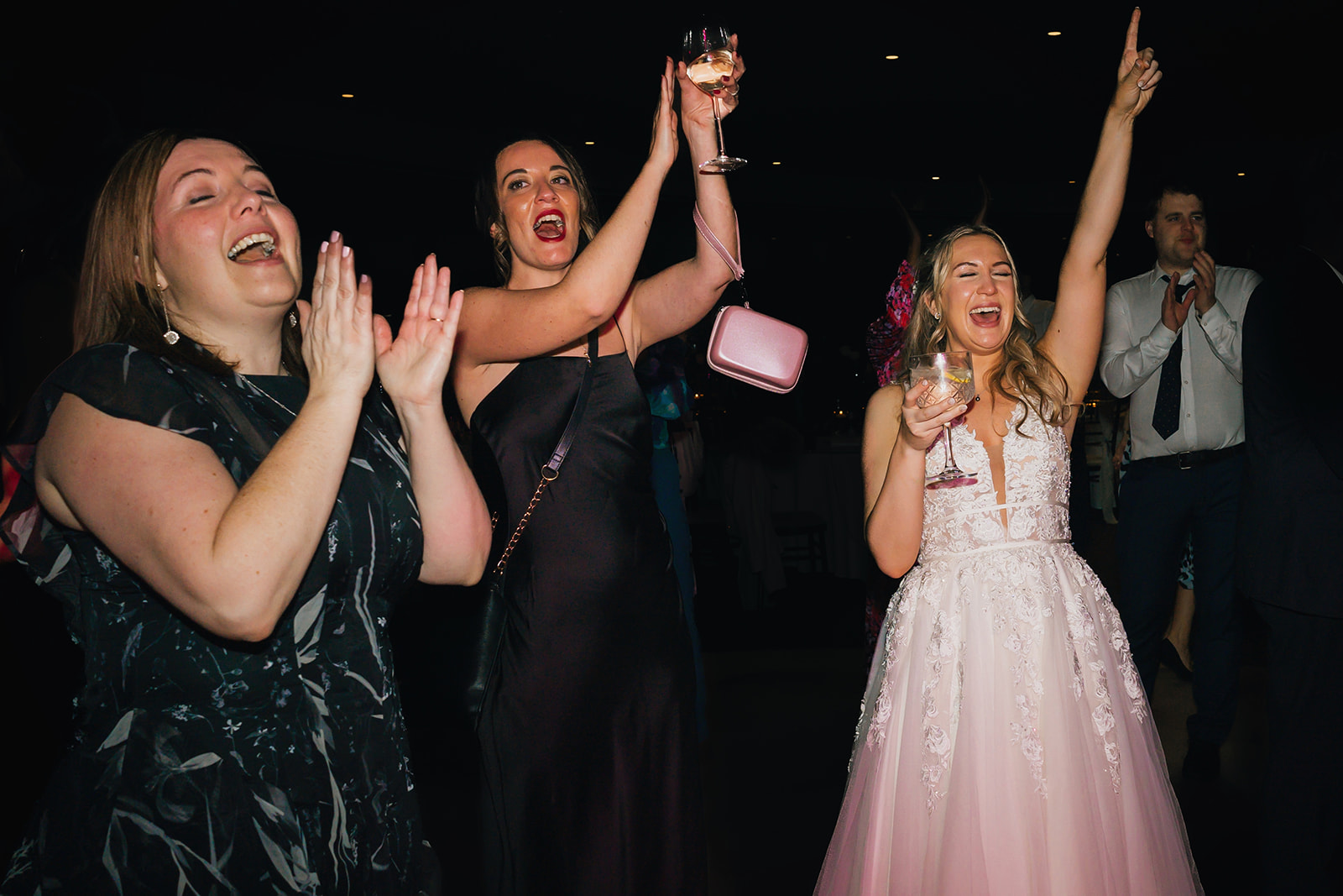 the bride and two wedding guests throw their arms in the air on the dance floor