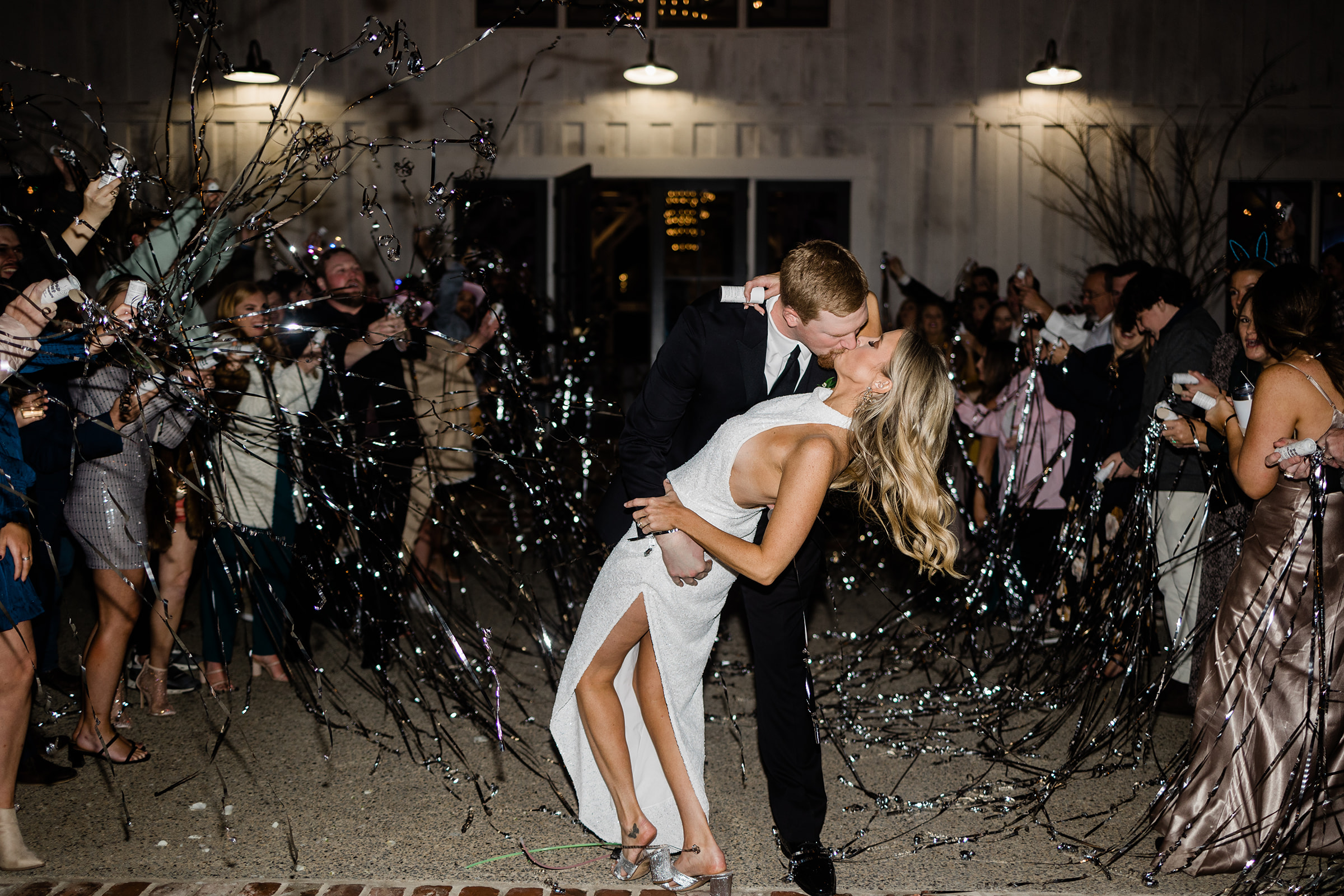 A explosive image of a bride and groom kissing, while the groom dips his bride and their guests spray streamers at them