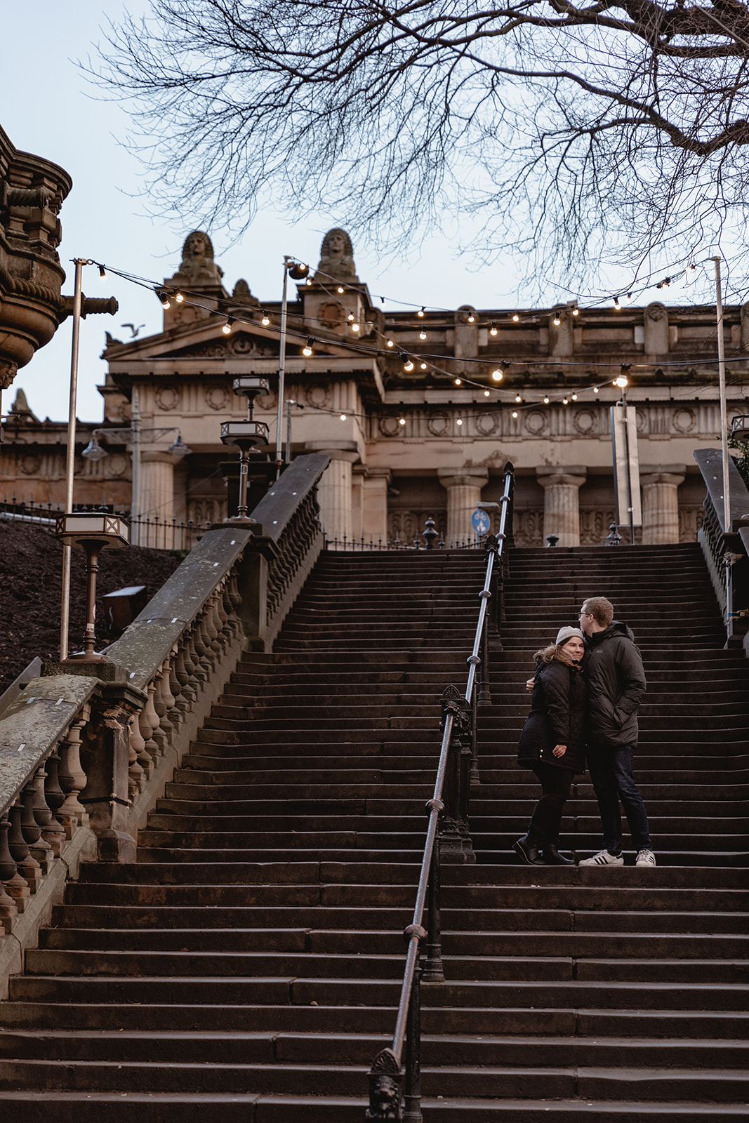 a couple standing on some stairs towards the city hugging