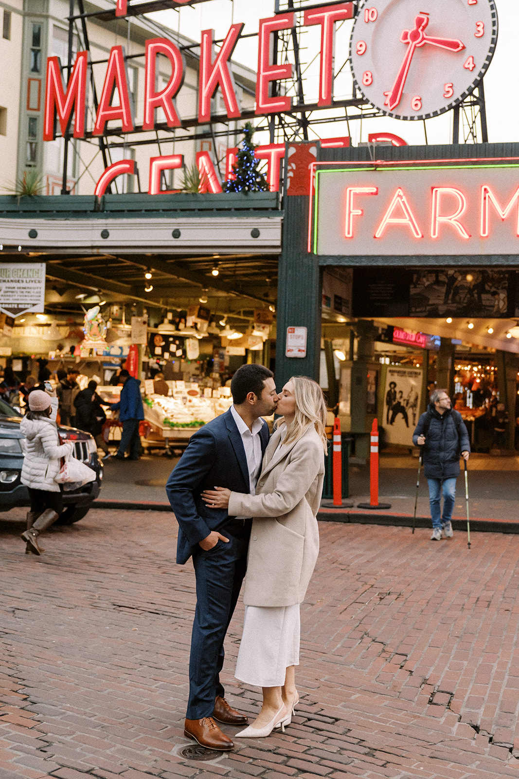 couple poses in front of Pike Place Market sign in downtown seattle during engagement session