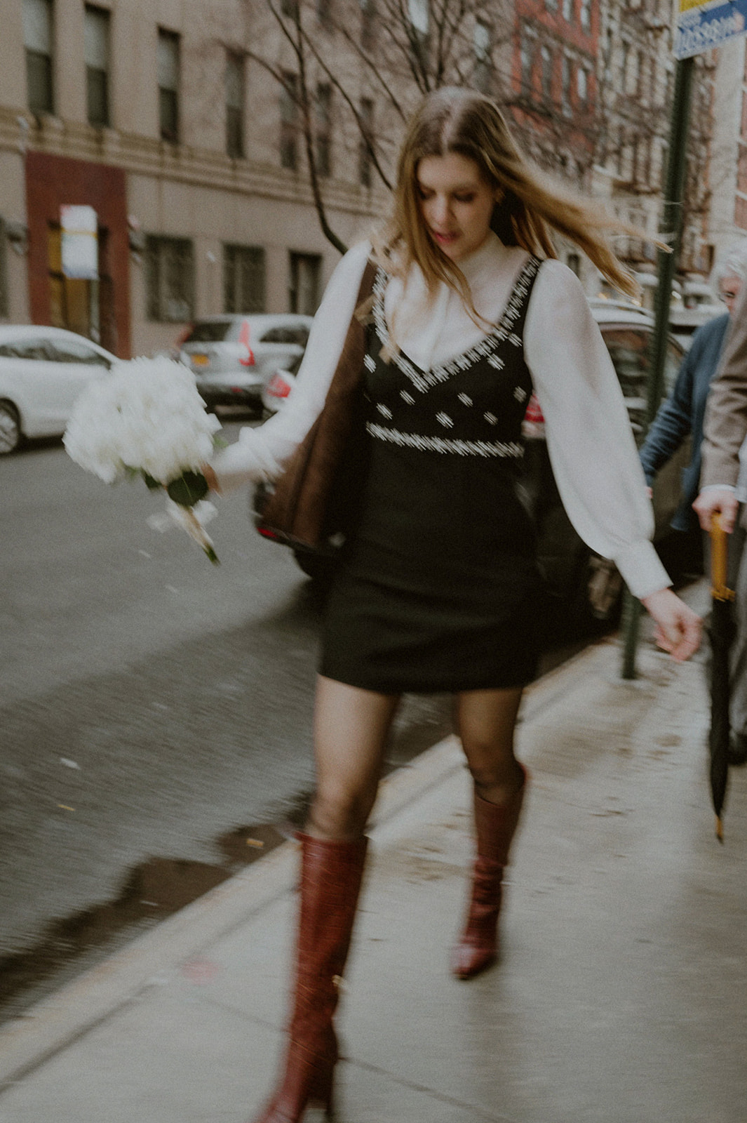 woman walking down the street in nyc in blurry picture while holding a bouquet of flowers