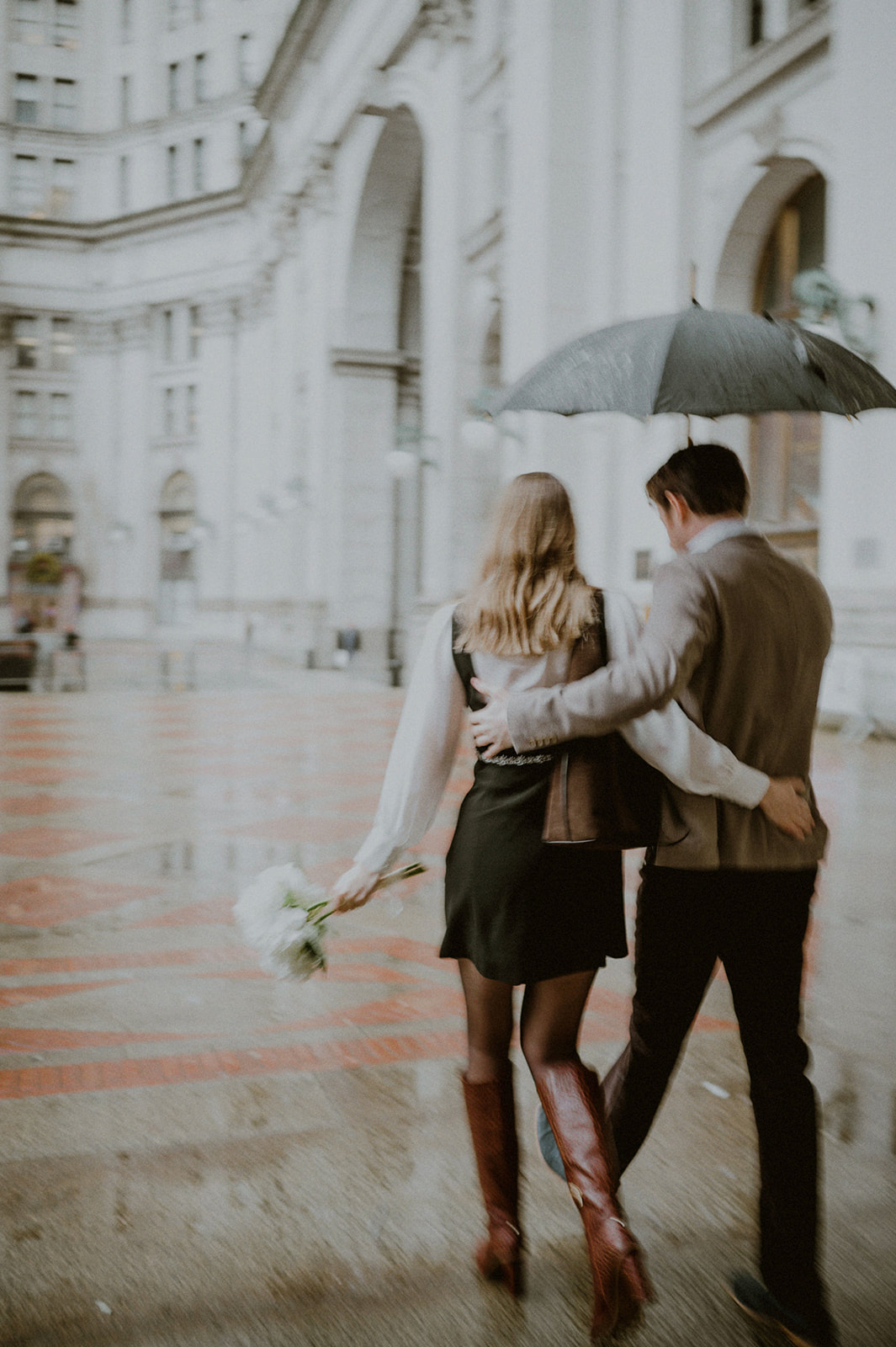 couple on their way to their city hall elopement in nyc holding an umbrella and a bouquet of flowers