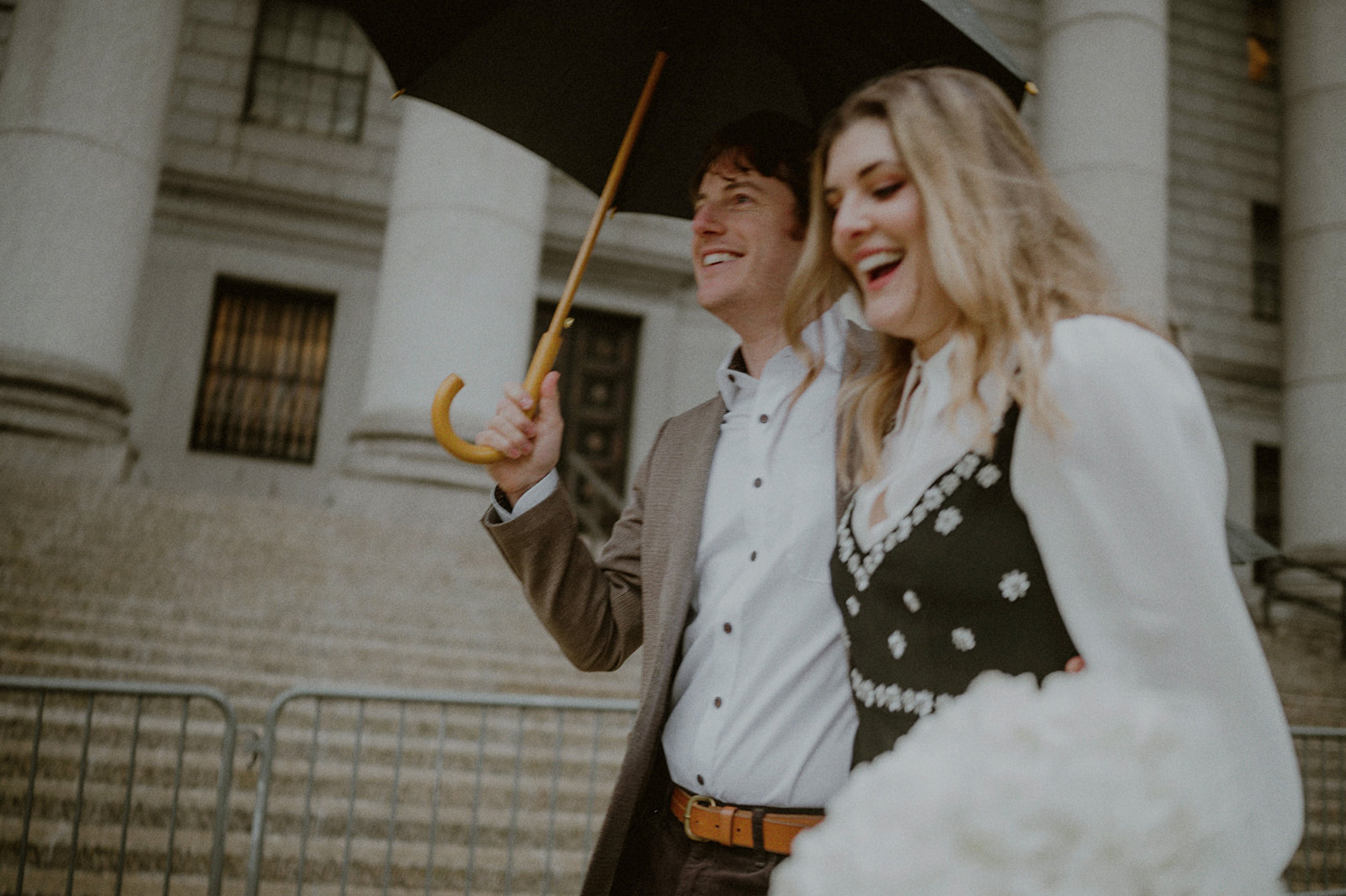 couple on their way to their city hall elopement in nyc holding an umbrella and a bouquet of flowers