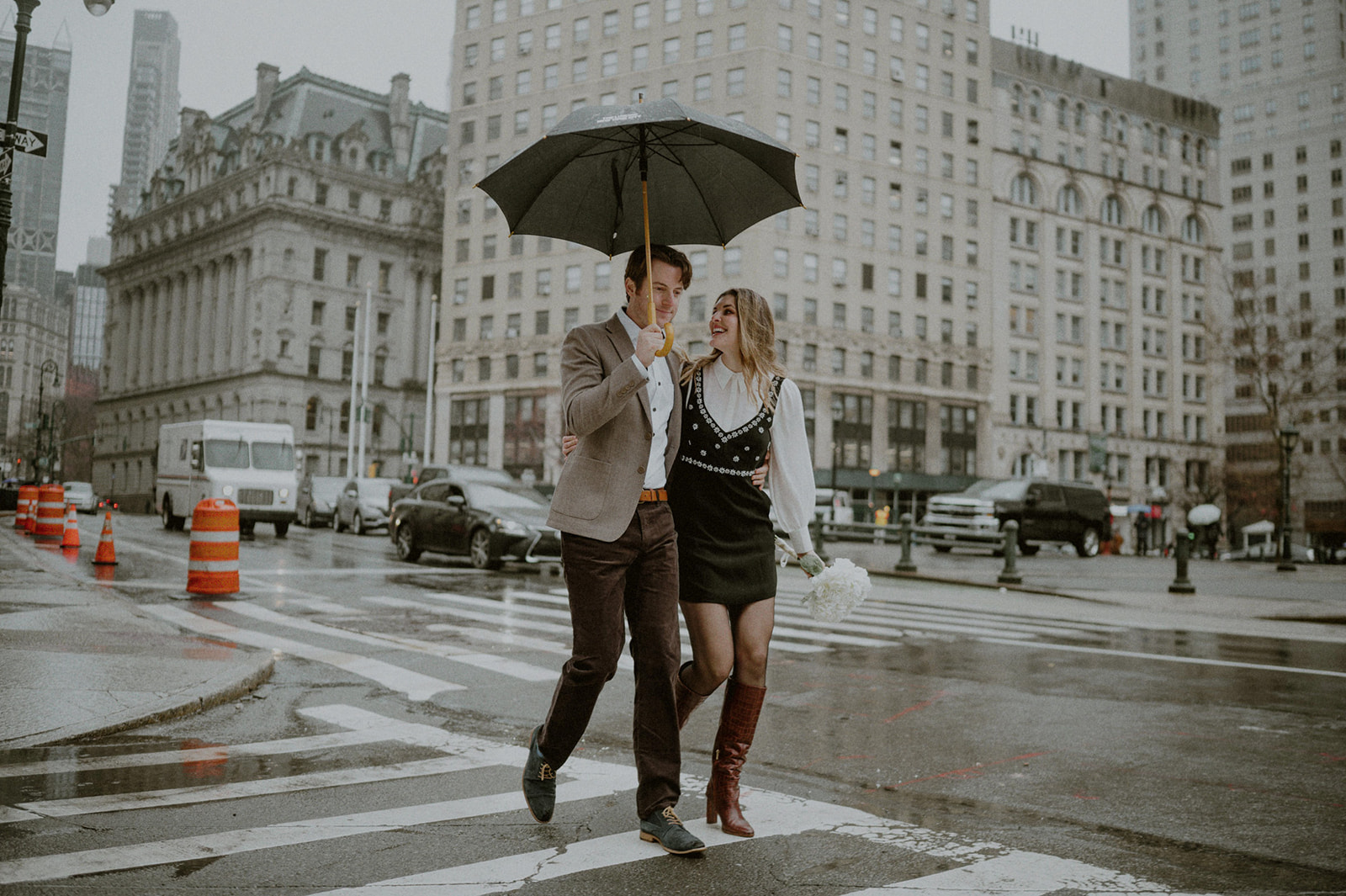 man and woman walking across rainy nyc street holding umbrella and laughing