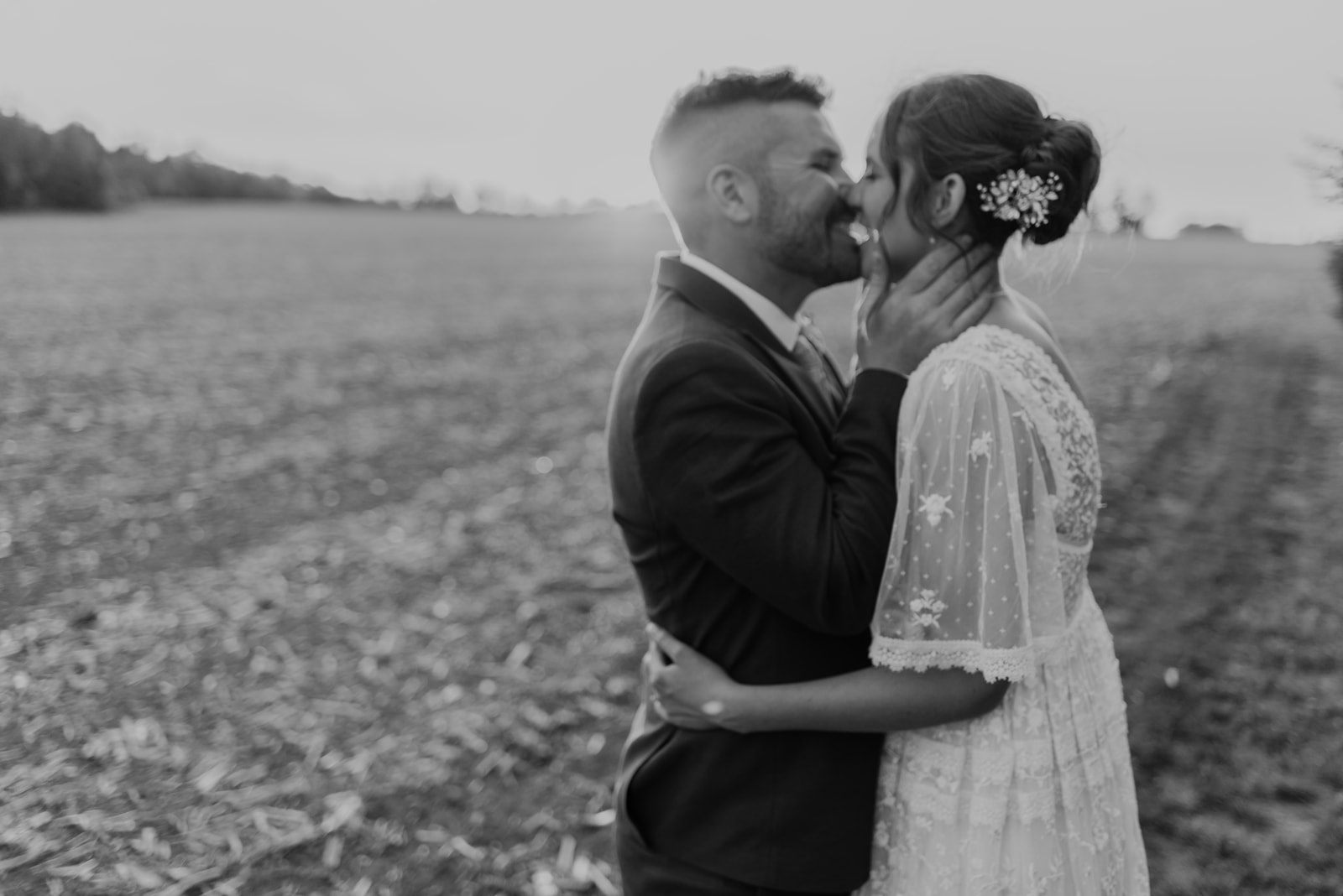 A newly wed couple share a kiss at sunset in a field. 