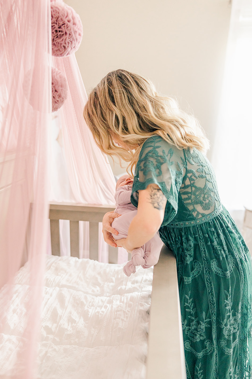 mother in green dress puts newborn in pink bed