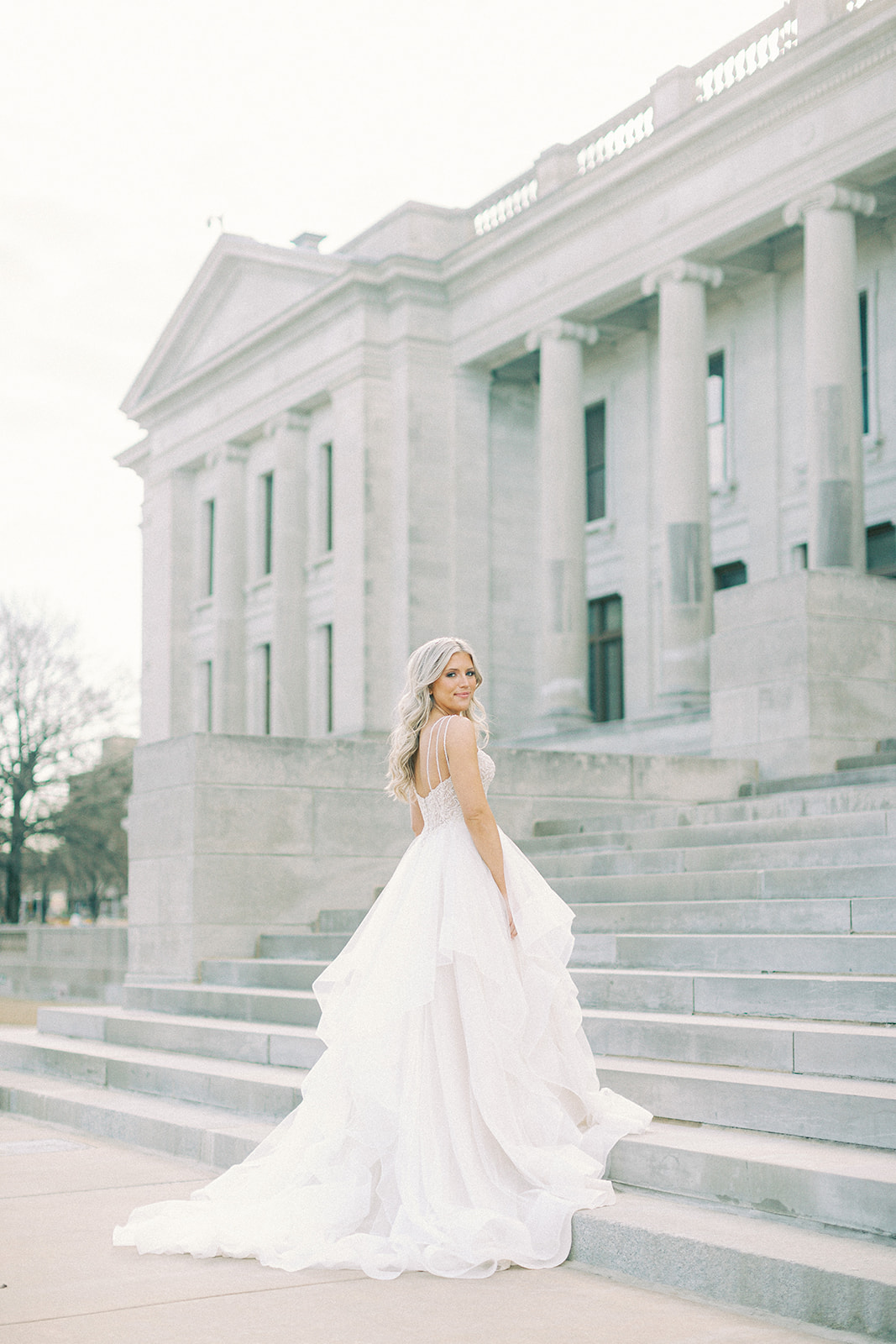 A bride standing on the steps in front of the Arkansas State Capitol in her wedding dress