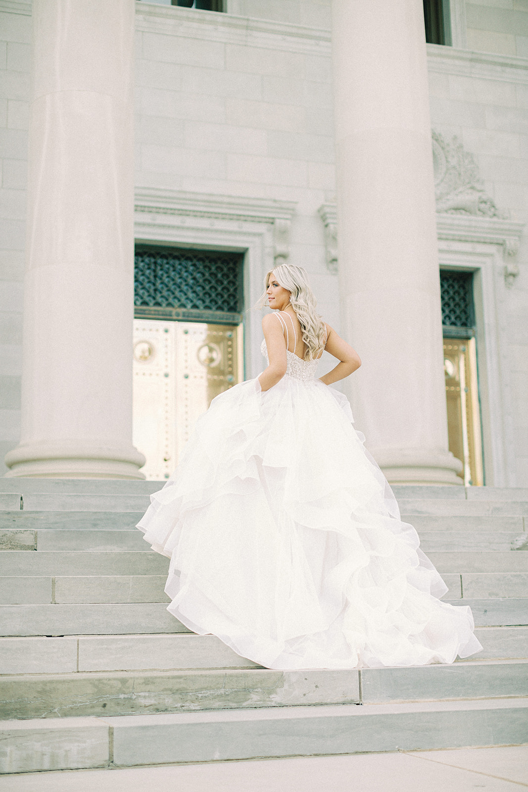 A bride standing on the steps in front of the Arkansas State Capitol in her wedding dress