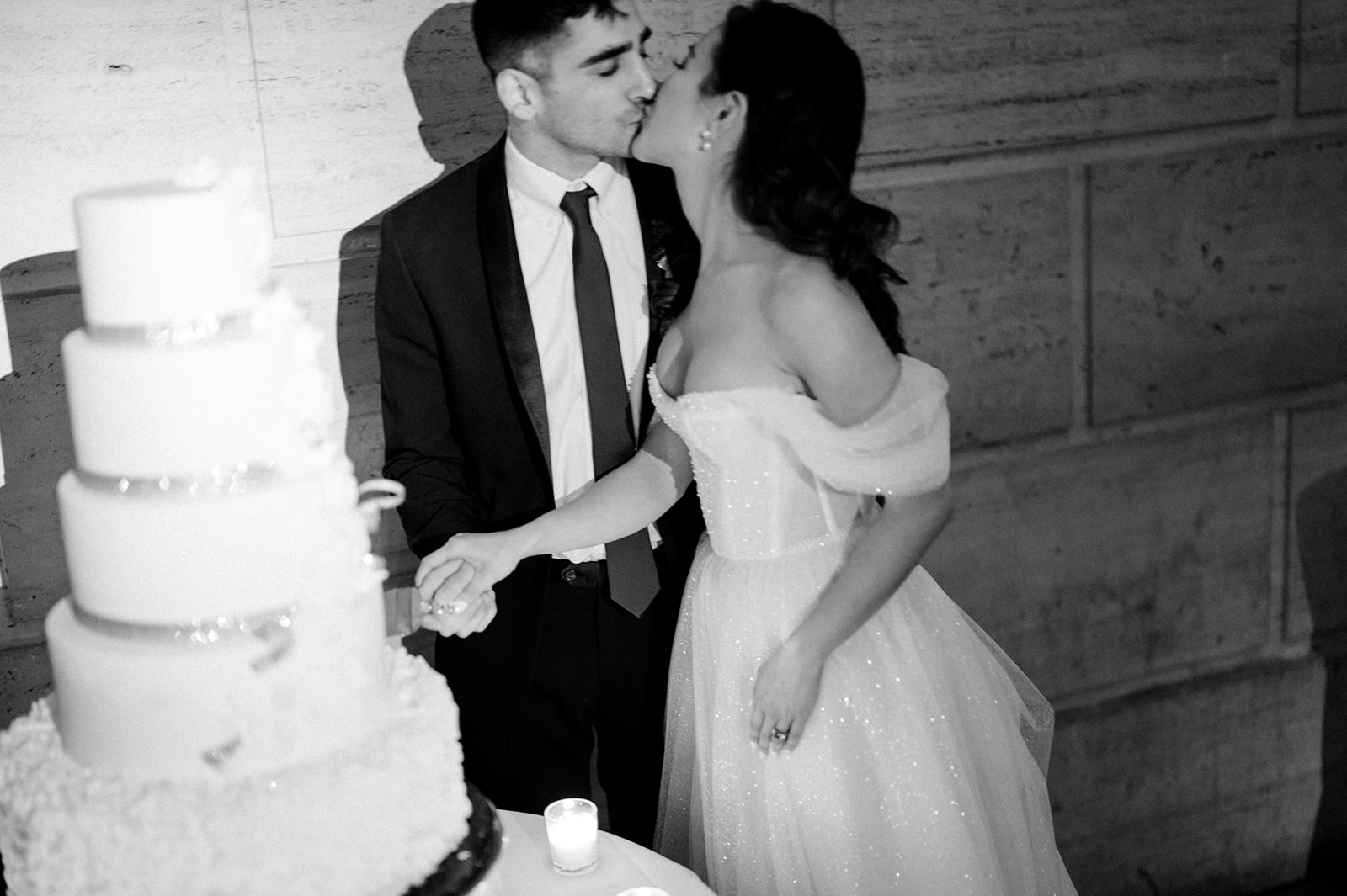 Black and white photo of bride and groom kissing while cutting cake at Winter Wedding at Philadelphia's Union Trust