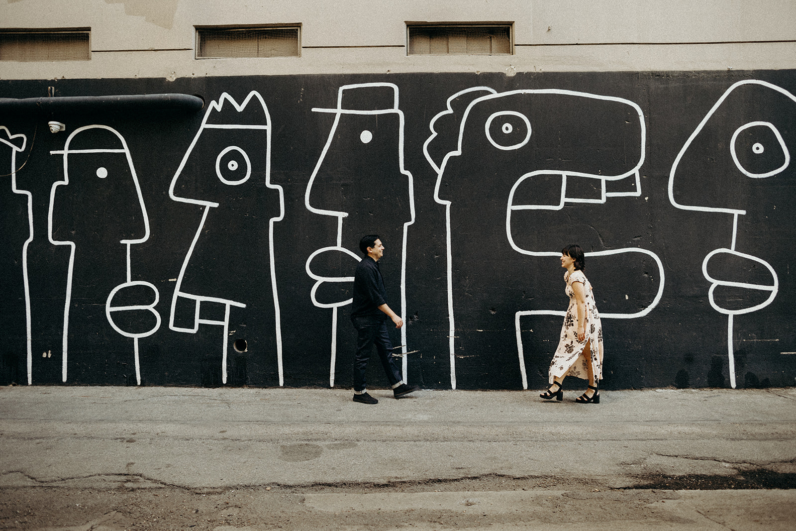 couple walking towards each other with black and white wall behind them
