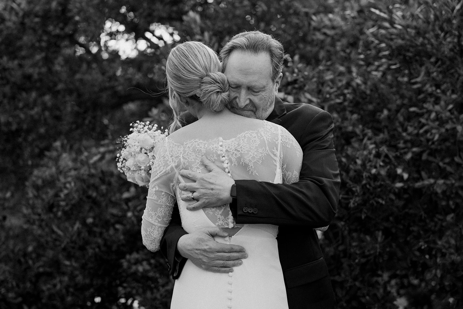 bride and older man hug while she holds white flower bouquet