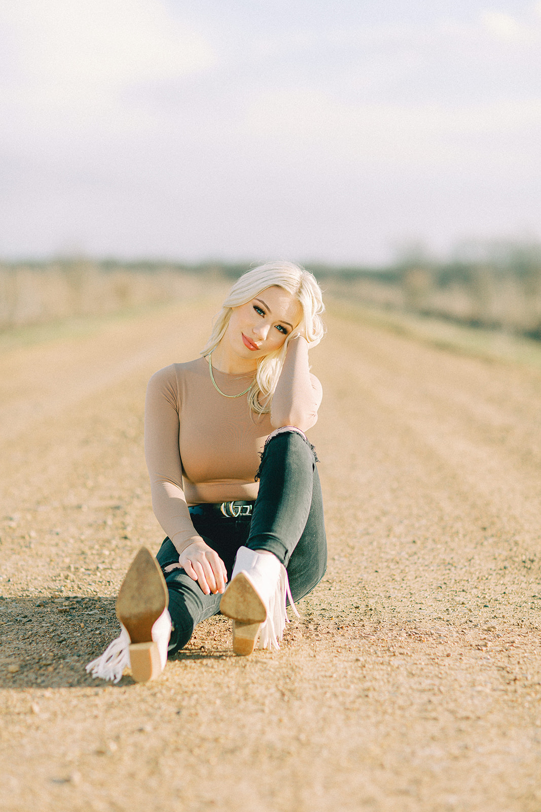 A senior girl poses by sitting on a dirt road in Texarkana, Texas