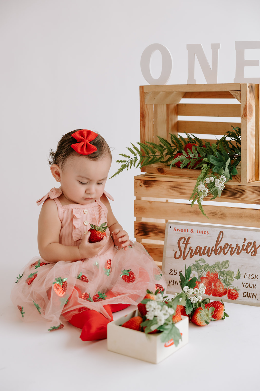 Strawberry-themed first birthday baby photoshoot in a natural light, white and bright, studio.