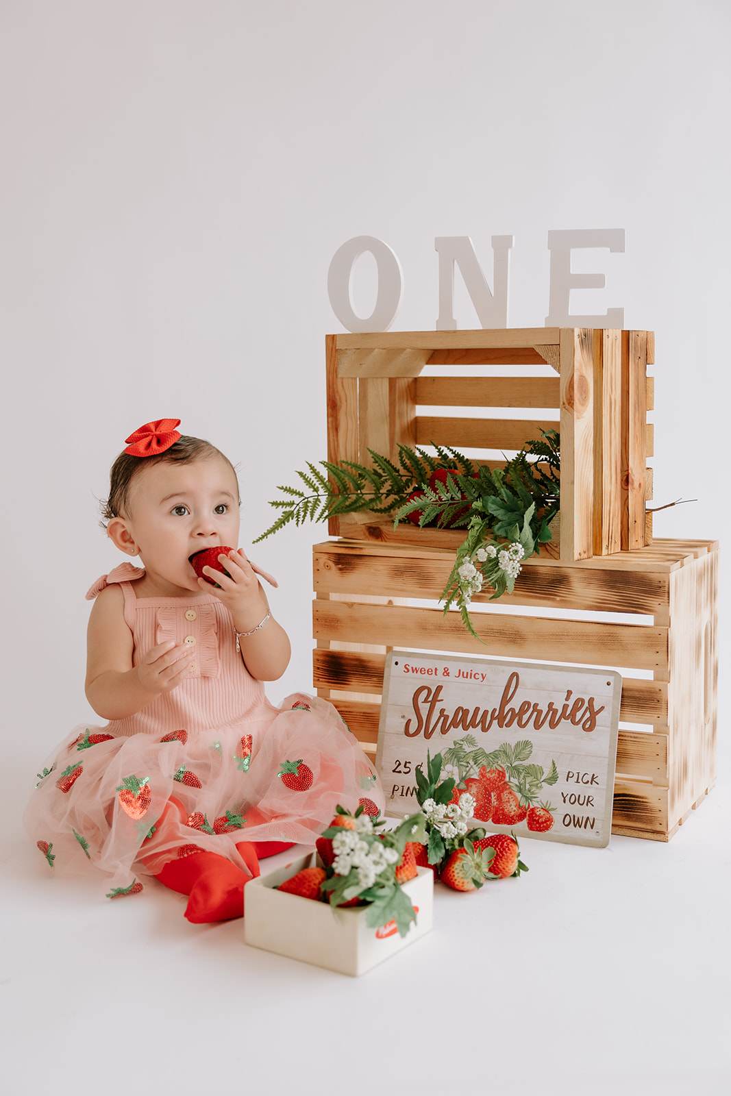 Strawberry-themed first birthday baby photoshoot in a natural light, white and bright, studio.