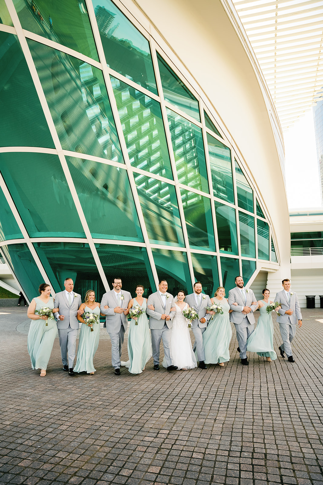 Wedding party links arms for a fun walk outside of the Milwaukee Art Museum