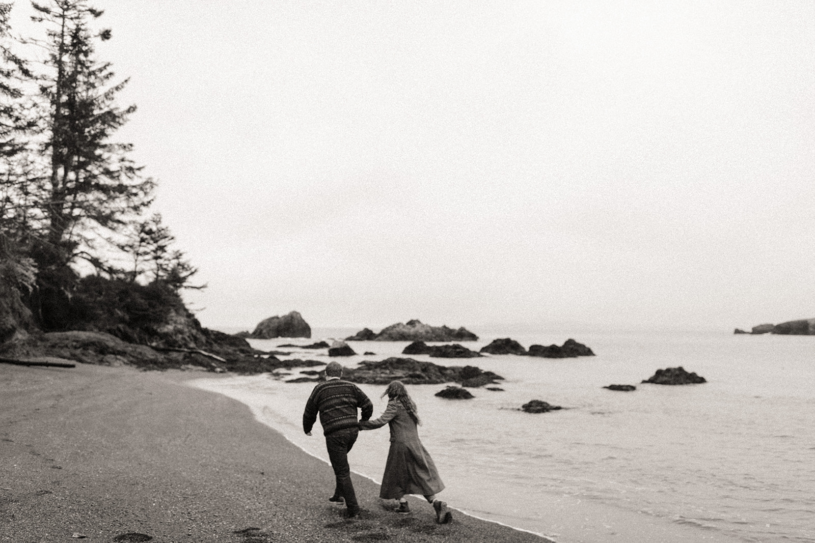 Couple running along the shoreline at Rosario Beach in Washington.