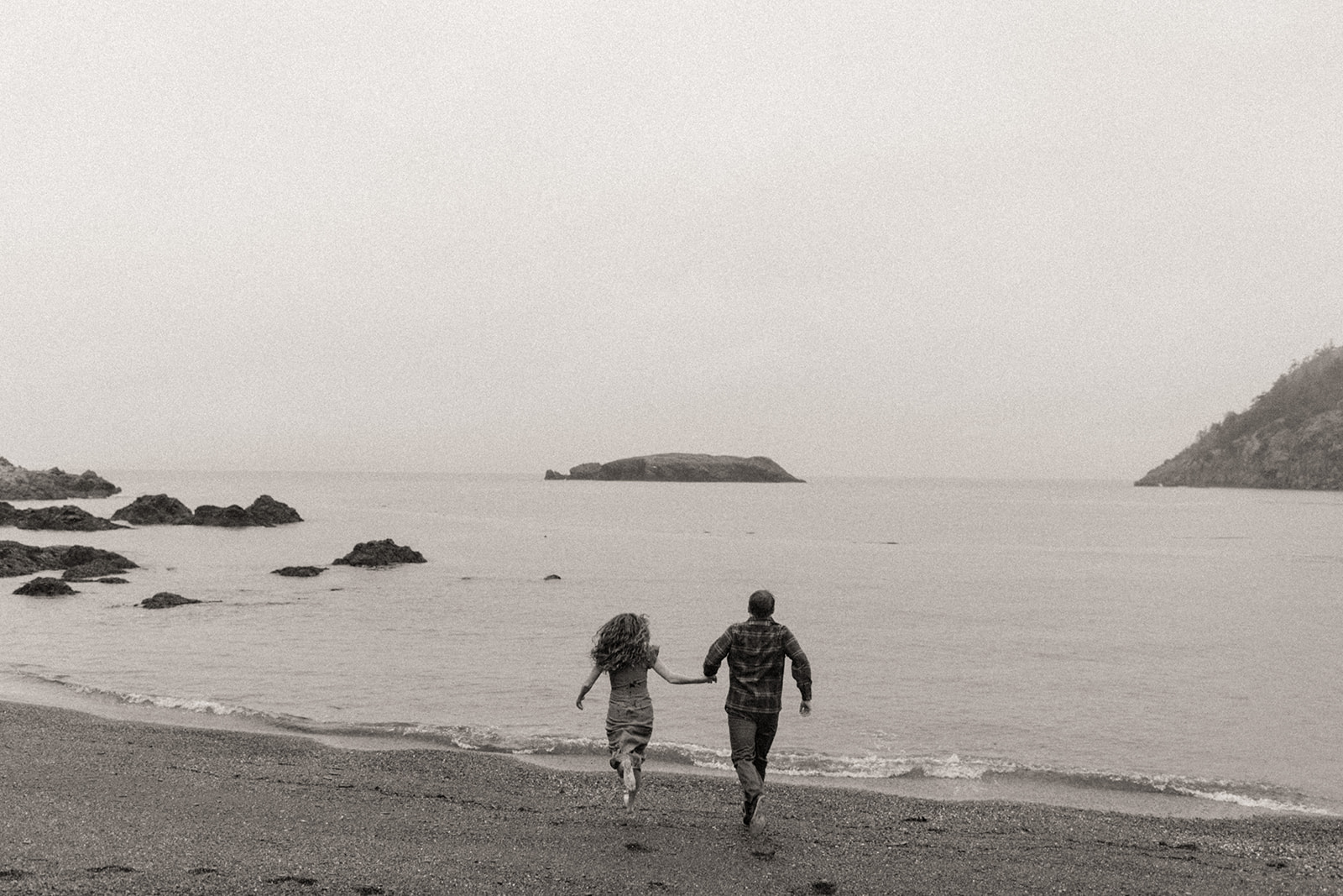 Couple running along the shoreline at Rosario Beach in Washington.