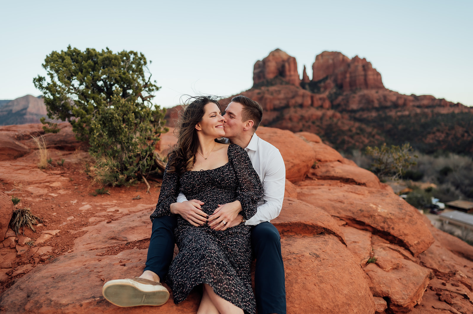 Man kisses wife's cheek while holding her in his arms with views of Cathedral rock in Sedona behind.