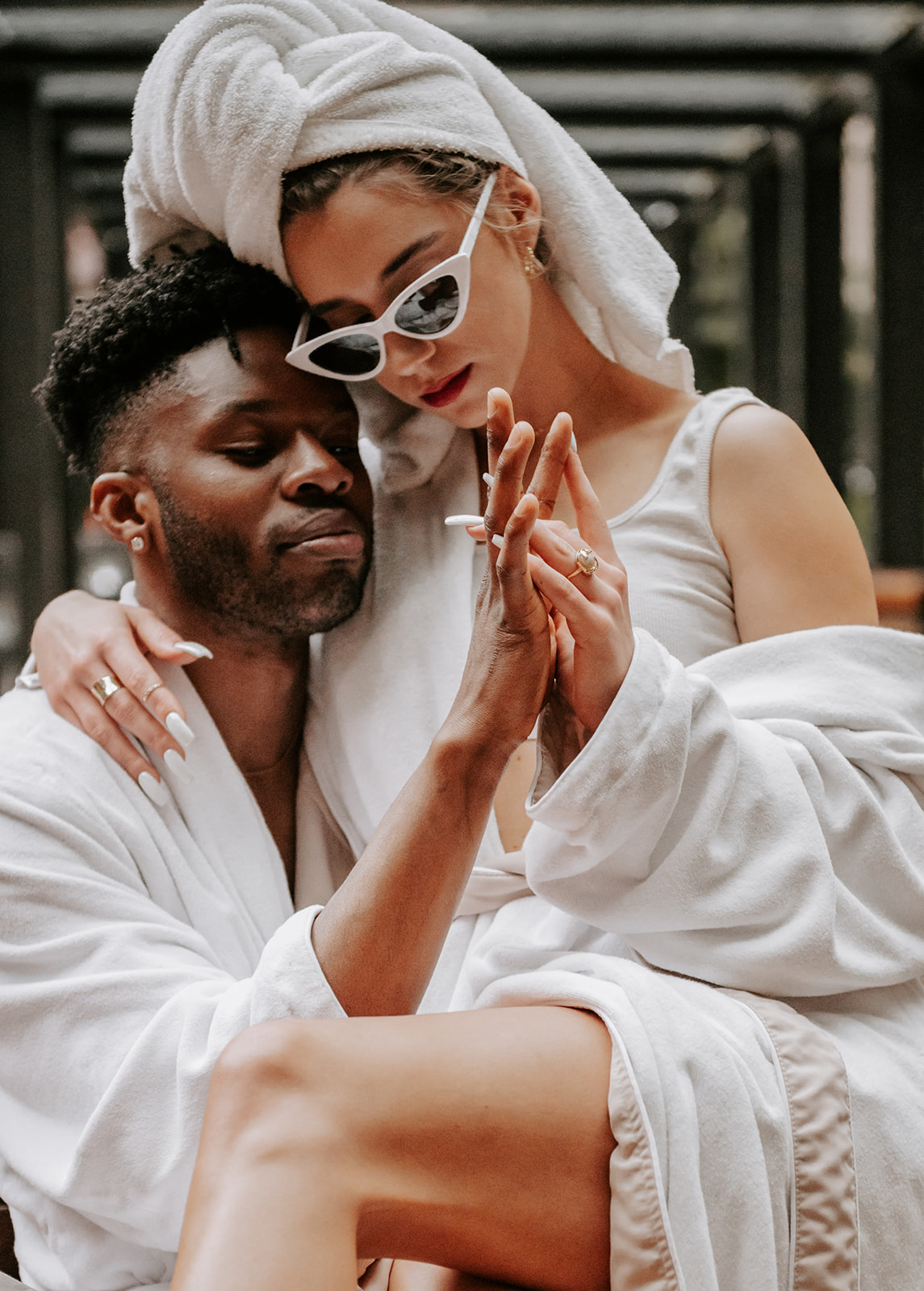 Couple embracing and Intertwining their hands. Wearing robes and she has a towel on her head and white sunglasses