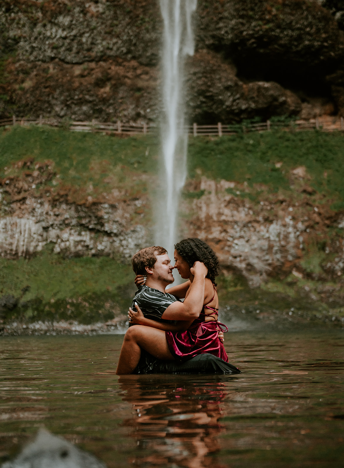 Engagement photos at silver falls of a couple sitting together in the water at the base of south falls