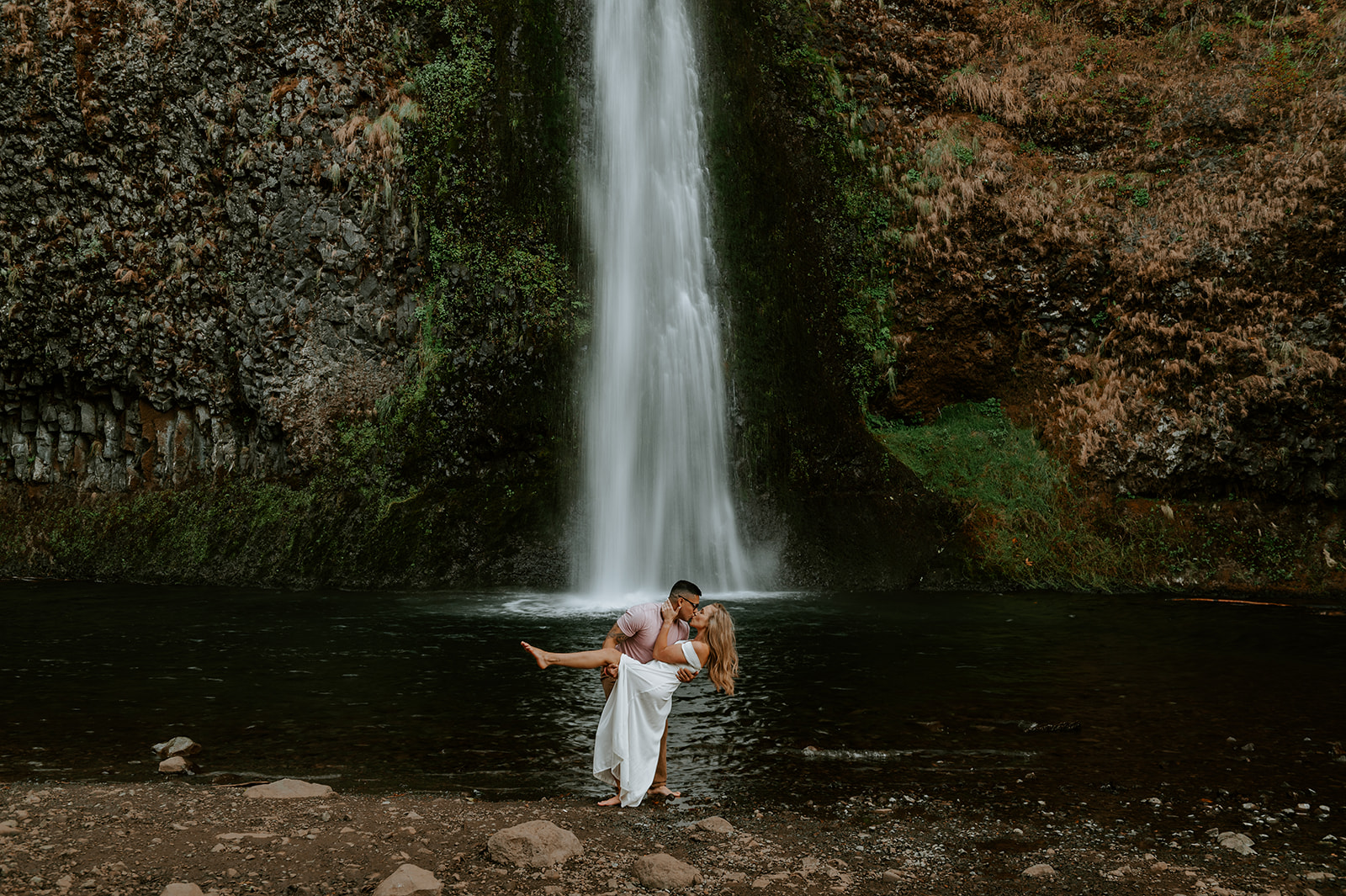 Couple kissing at the base of horsetail falls in the Colombia river gorge. Guy dipping the girl