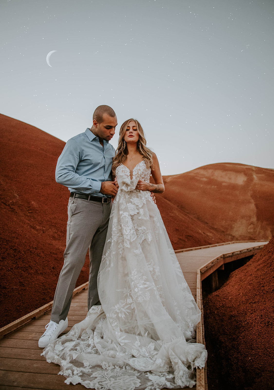 A bride clutching her wedding dress on the bridge at the painted hills with the moon and stars in the sky 