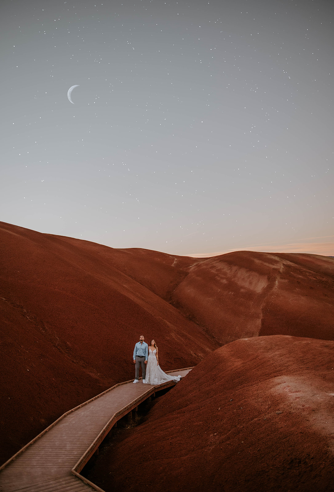 A couple who just eloped looking up at the moon and stars on the bridge at the Painted Hills