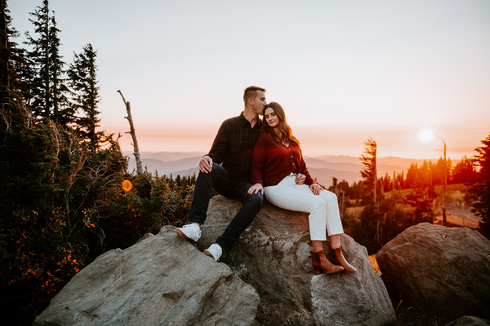 Couple sitting on a rock nuzzled up together watching the sunset for engagement photos