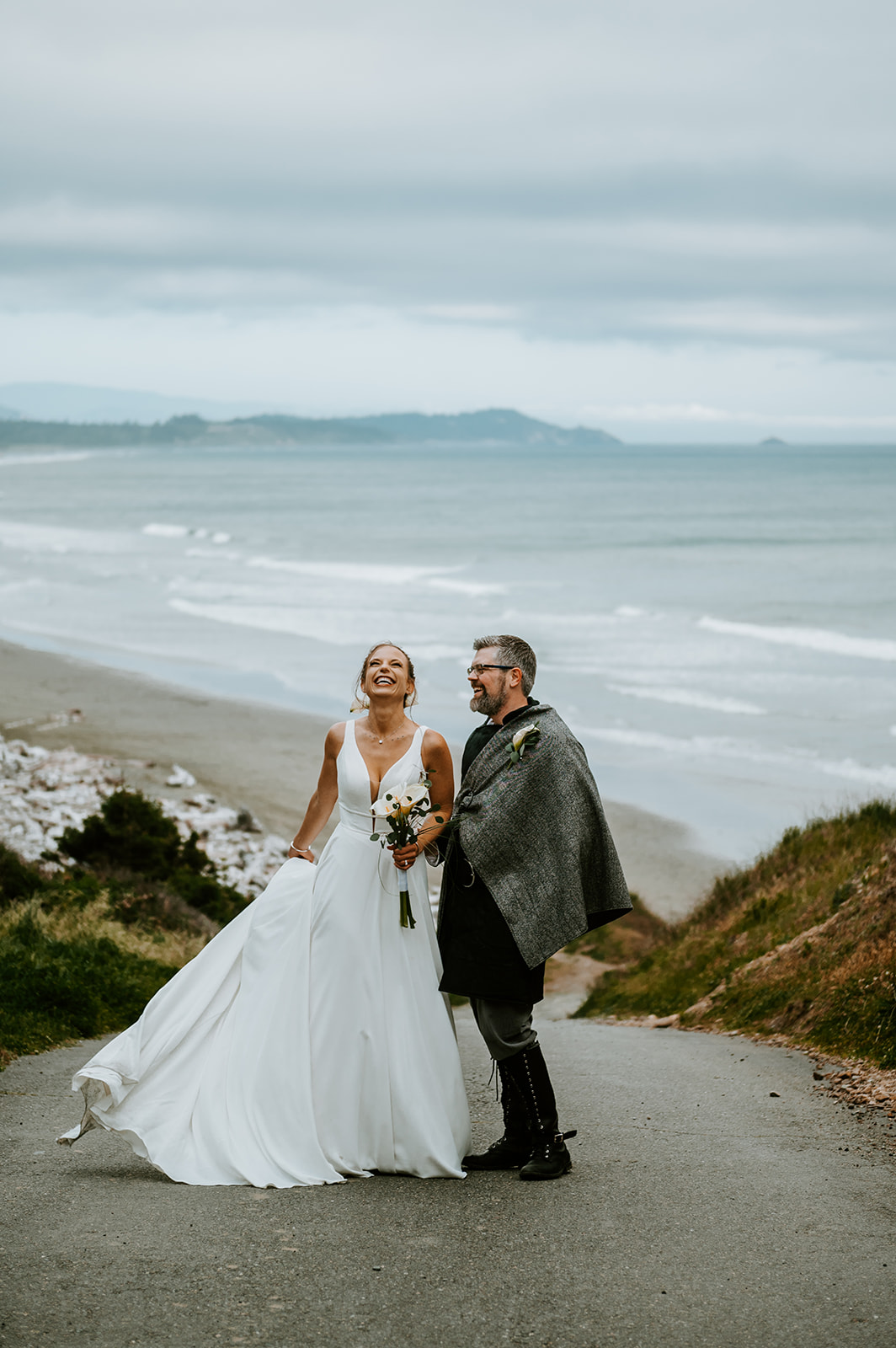 Bride and groom smiling together while the bride twirls her dress overlooking the Oregon coast