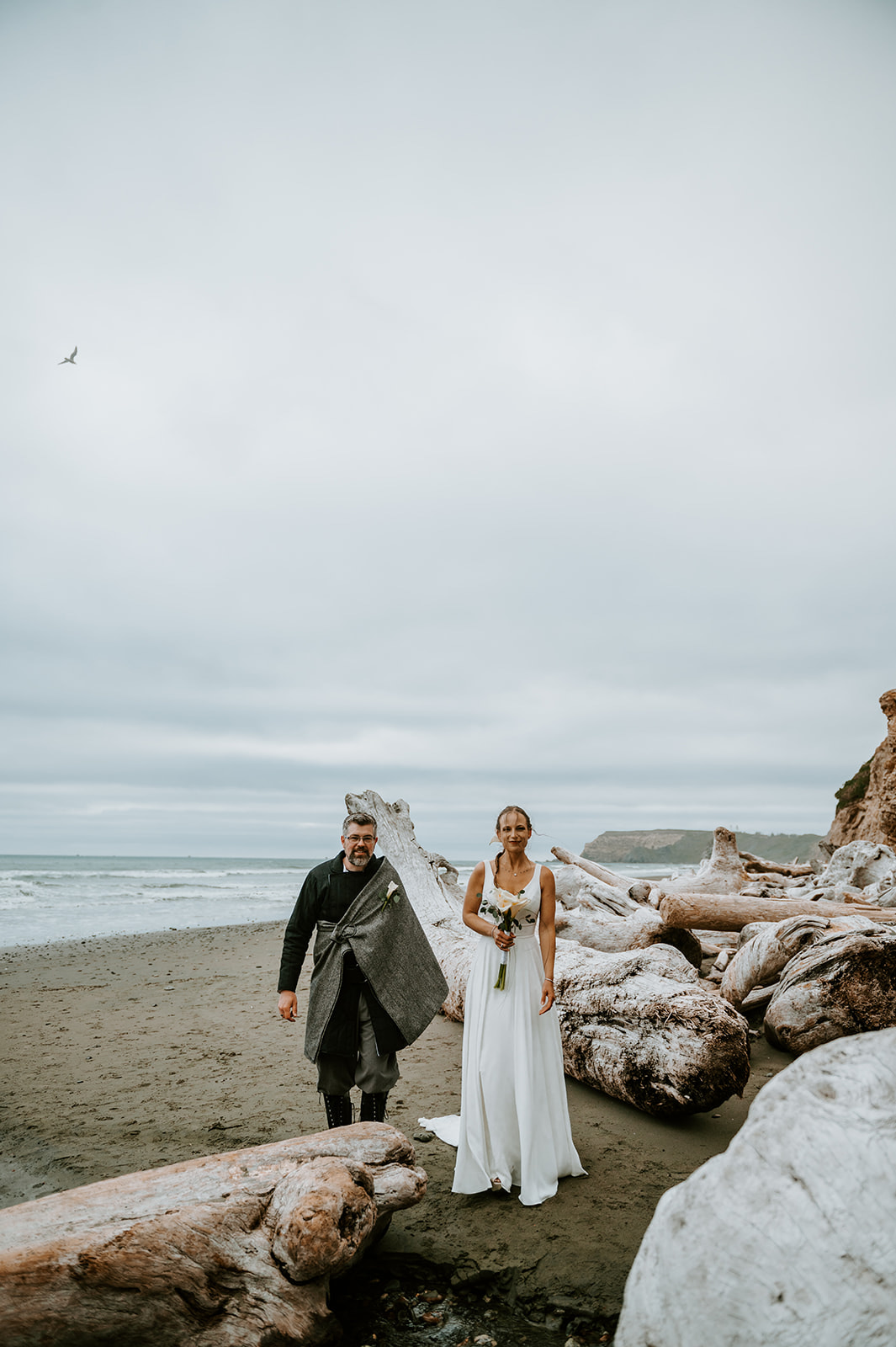Bride and groom standing on a driftwood beach on the Oregon coast