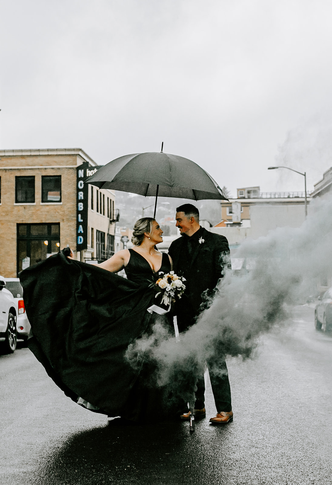Bride and groom in all black kissing under an umbrella with a black smoke bomb at the ruins at the astor