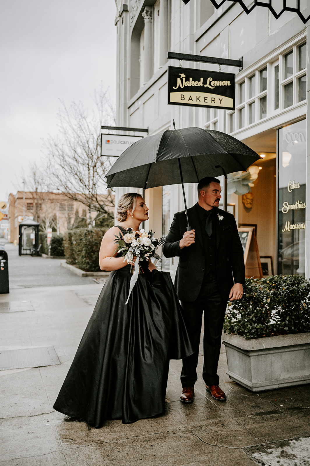 Bride and groom in all black with an umbrella during their wedding at the ruins at the astor