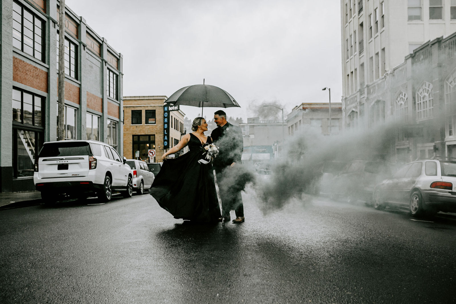 An edgy and groom in all black with a black smoke bomb and an umbrella on the streets of Astoria