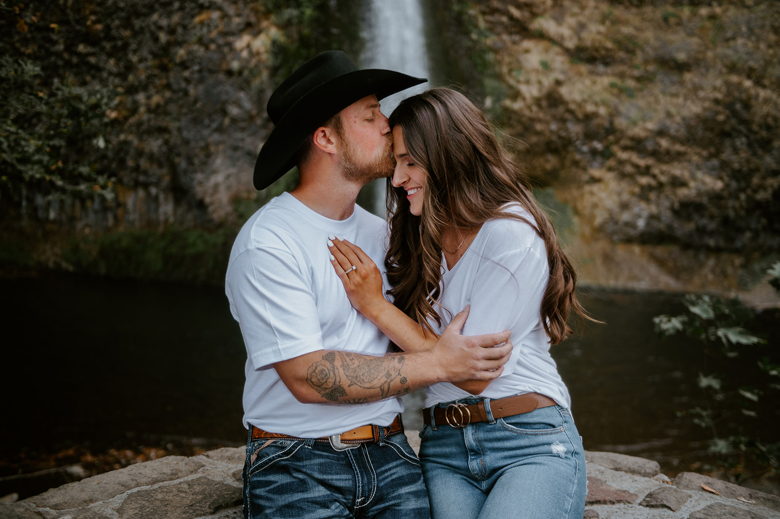 Casual couple where man is kissing woman’s forehead at the base of horsetail falls in oregon