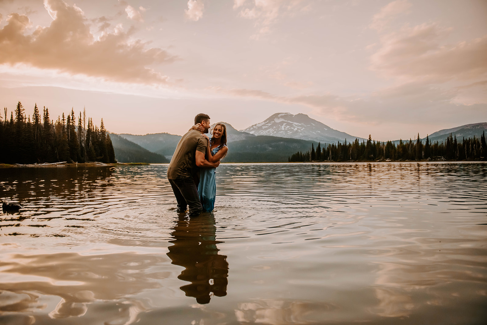 A couple playing in the water and kissing in front of the mountain at sunset