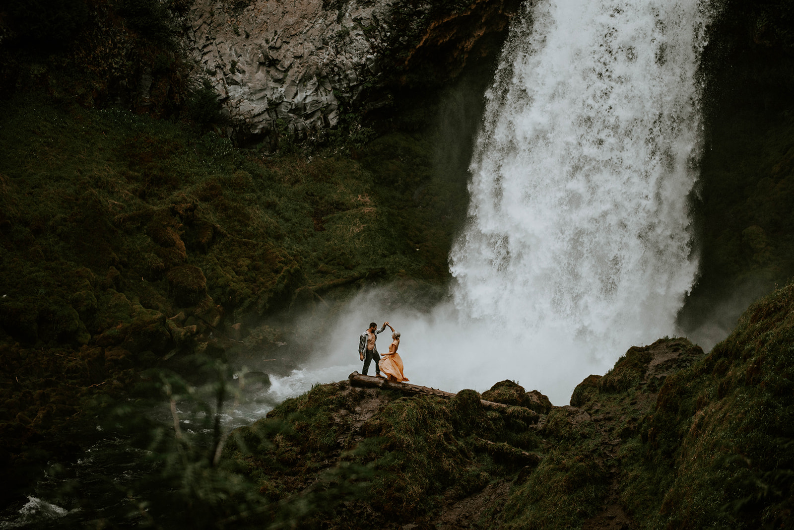 A couple dancing together at the base of a waterfall for their engagement photos