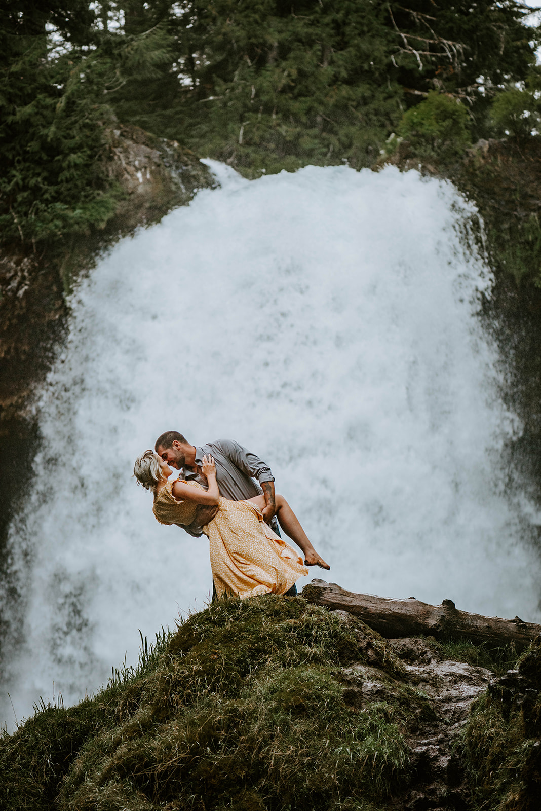 A man dipping his fiance during engagement photos in front of Sahalie Falls
