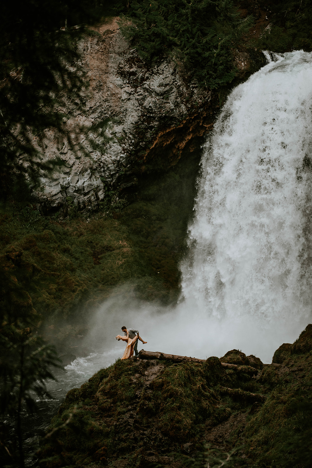 A man dipping his fiance at the base of an Oregon waterfall 