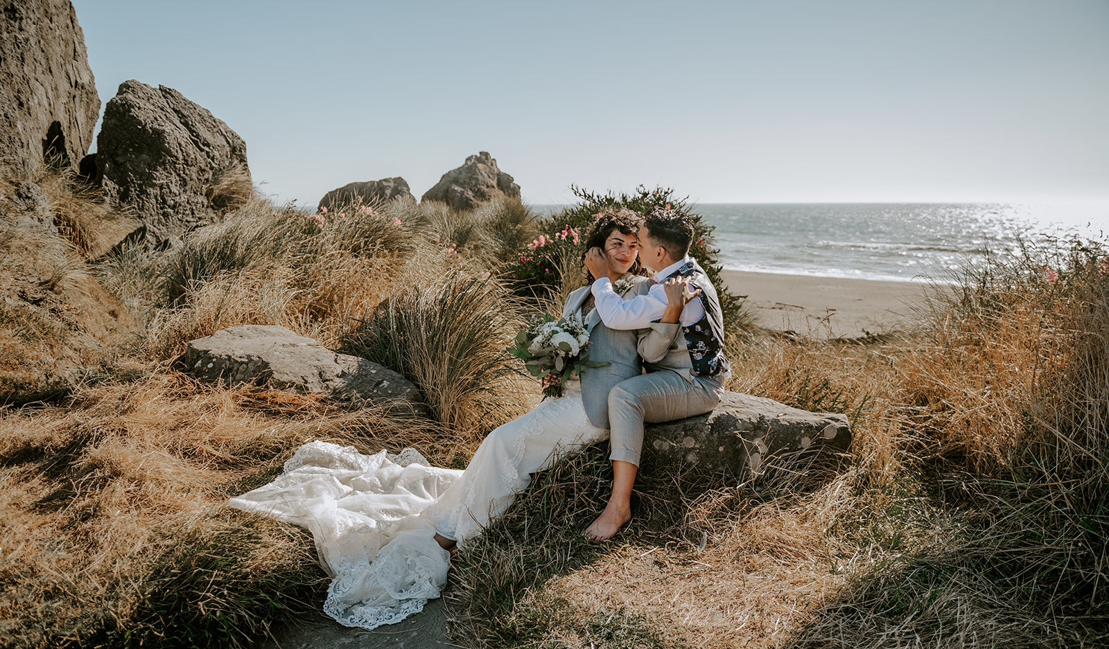 Two brides embracing at kissing rock on the Oregon coast With the beach in the background