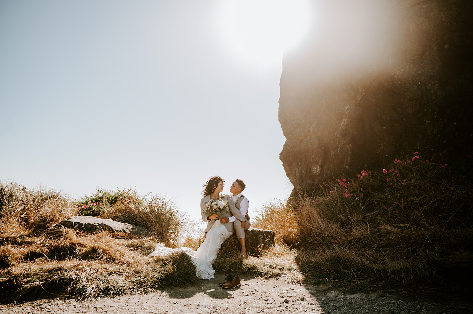 Two brides kissing at kissing rock on the Oregon coast With the beach in the background At sunset