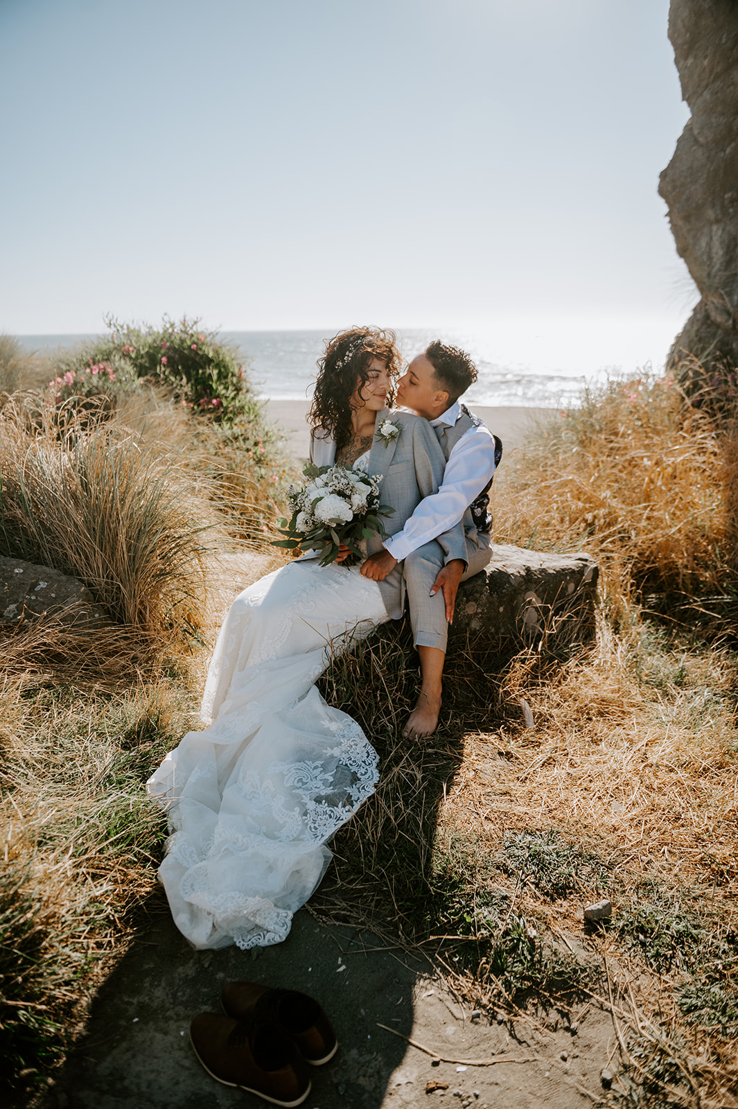 Two brides kissing at kissing rock on the Oregon coast With the beach in the background