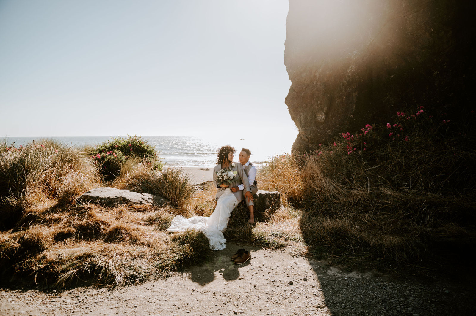 Two brides at kissing rock with wildflowers and the Oregon coast in the background