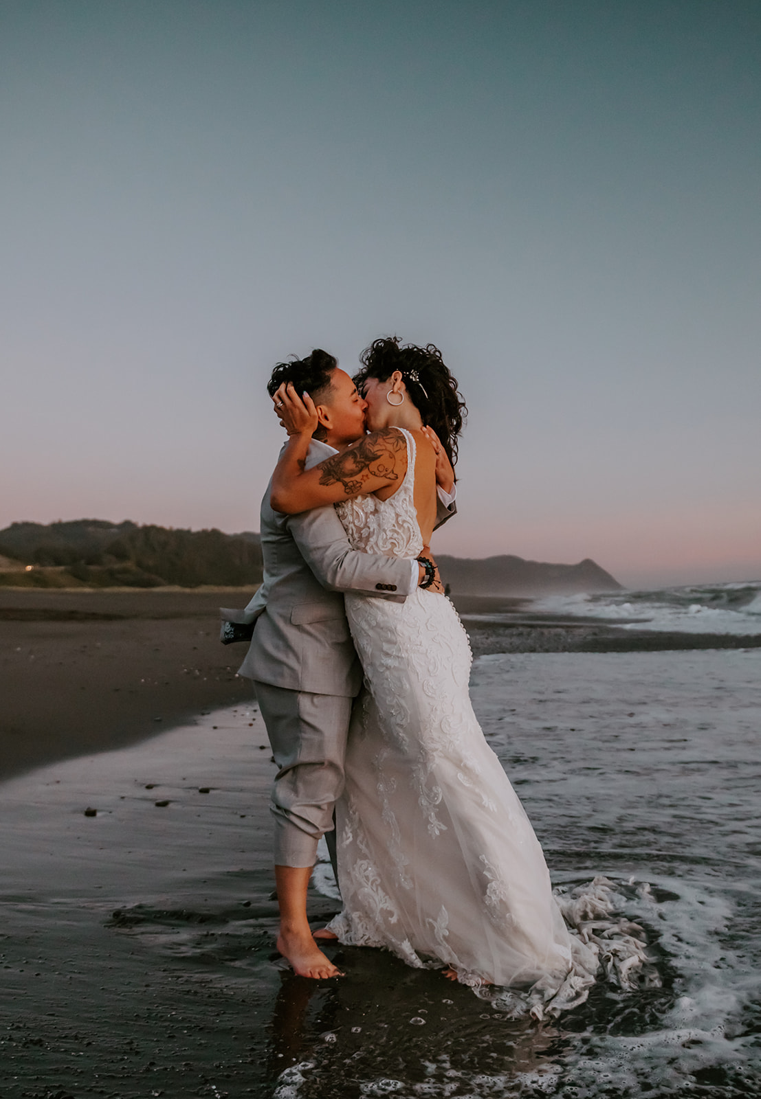 Two brides kissing in the ocean on the Oregon coast after sunset