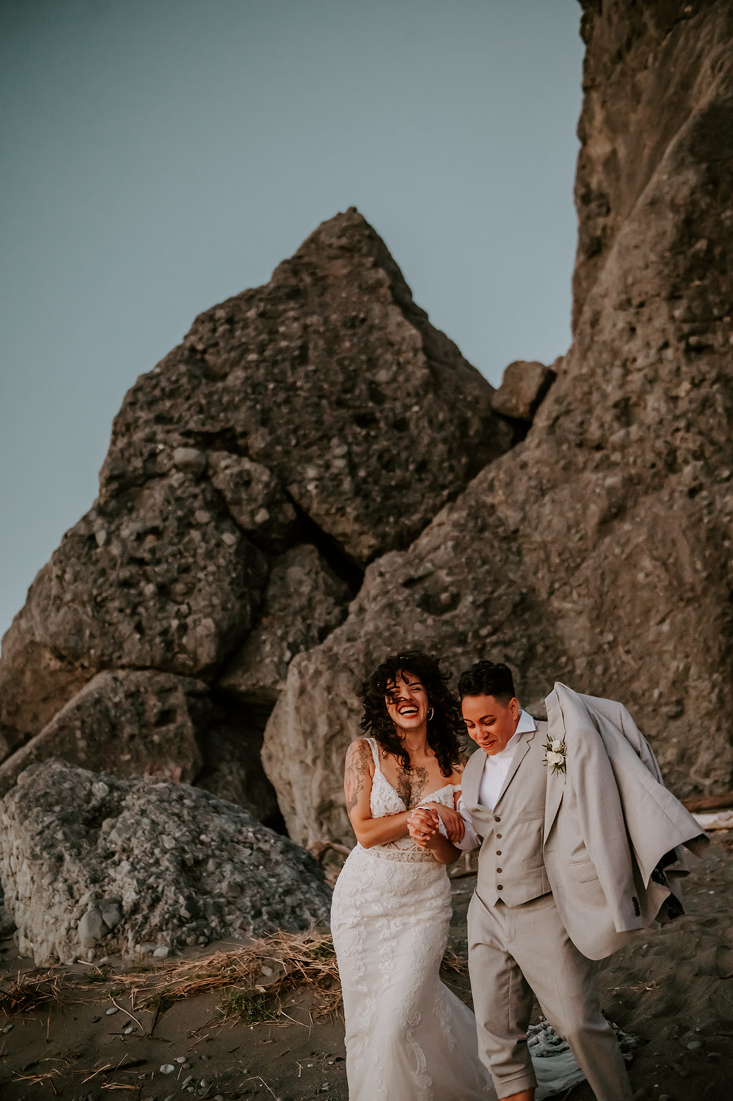 Two brides running on the beach kissing rock on the Oregon coast