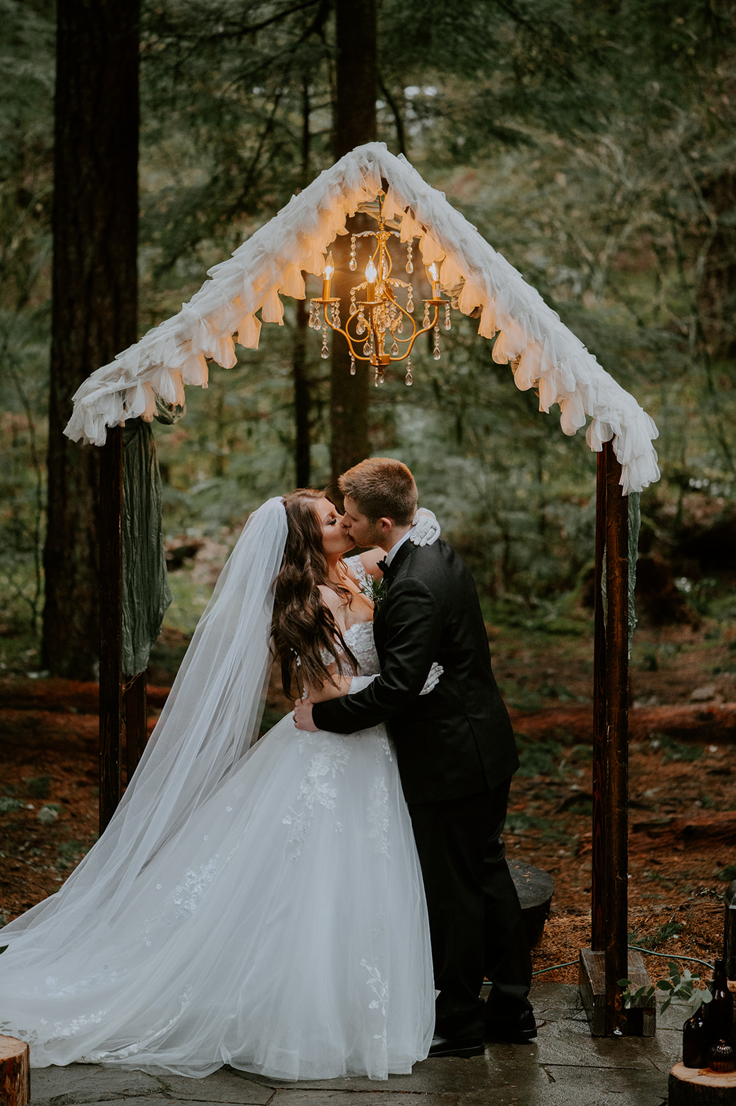 Bride and groom kissing under their DIY wedding alter with a chandelier at their intimate ceremony in Oregon woods