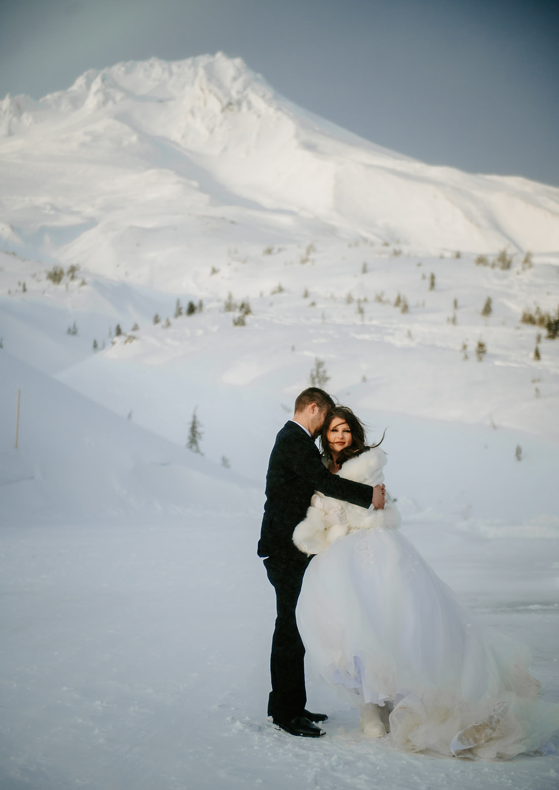 Bride and groom embrace on Mt. Hood during a winter storm on their wedding day.