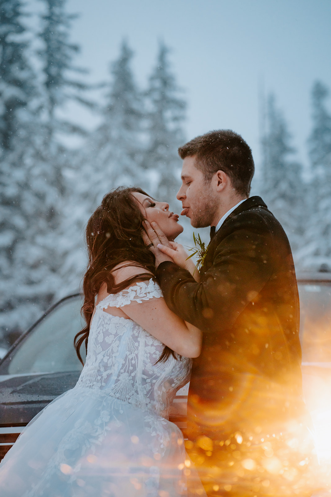 Bride and groom sticking their tongues out at each other in front of headlights during a snowstorm on Mt. Hood