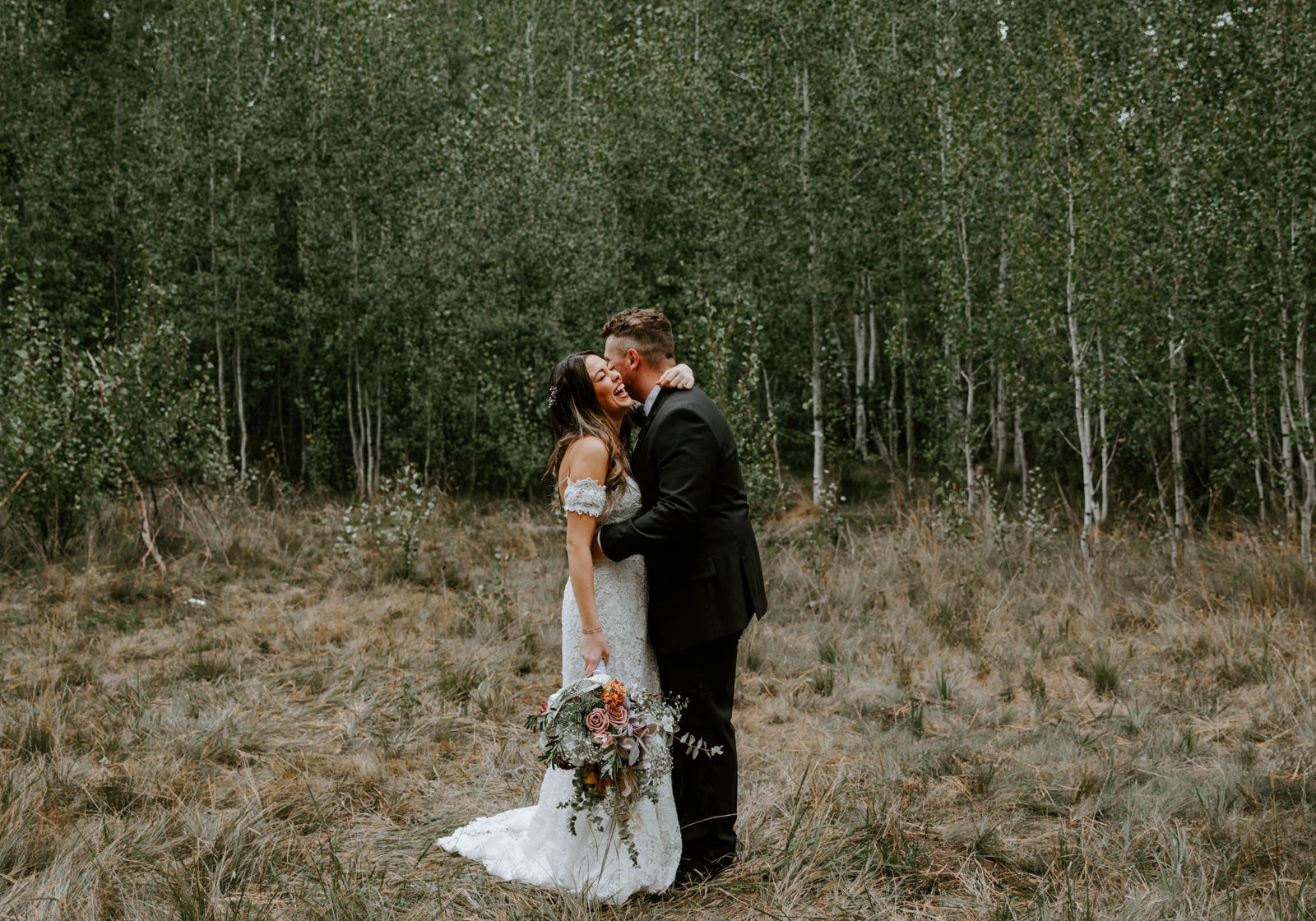 Bride and groom hugging in front of the aspen groves at shevlin park while the bride laughs