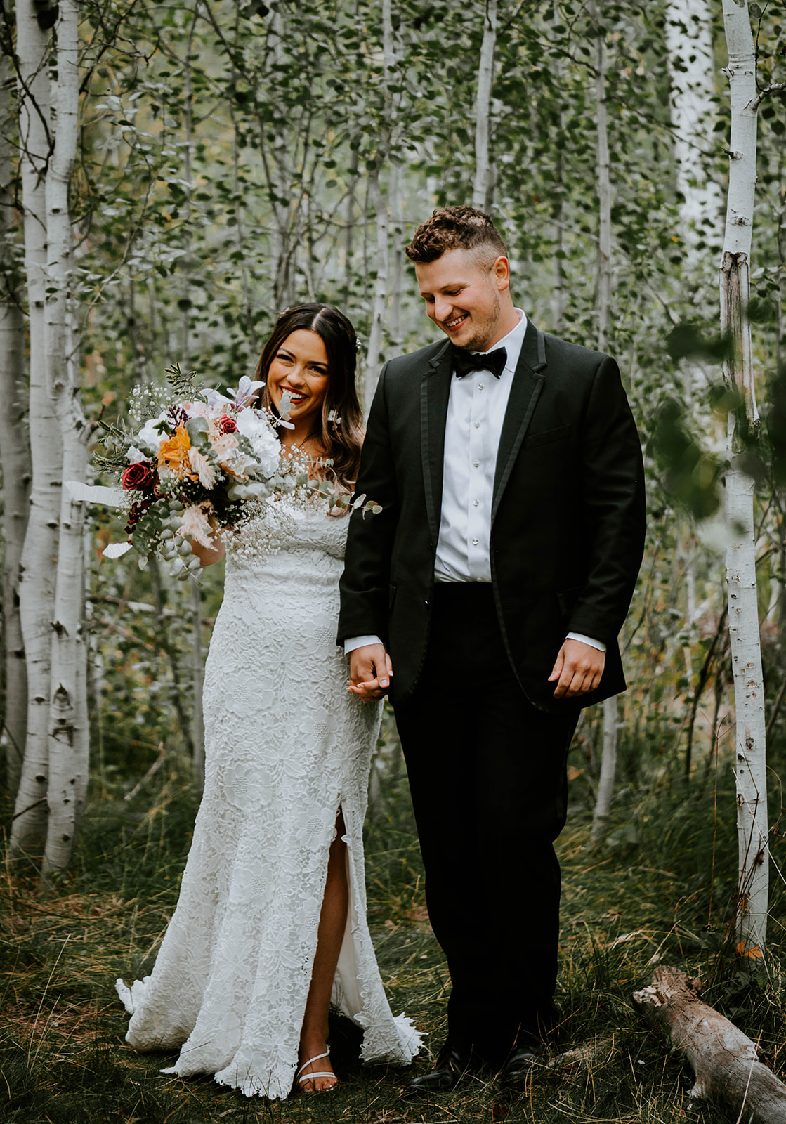 Bride and groom walking through aspen trees while bride points her bouquet at the camera