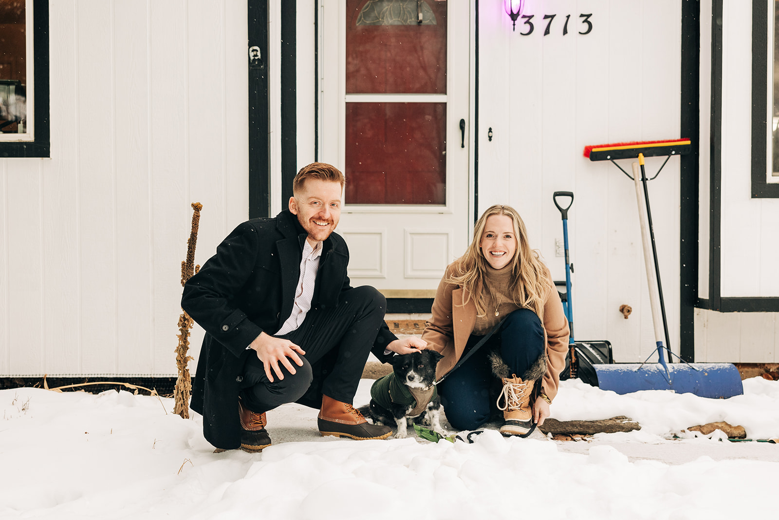 man and woman crouching in front of their house with their dog